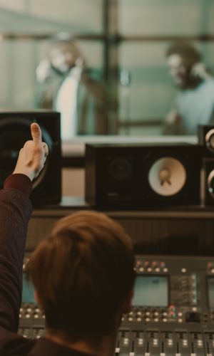 sound producer showing thumb up to singers behind glass at recording studio sound producer showing thumb up to singers behind glass at recording studio